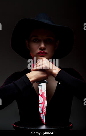 Mädchen mit einem riesigen blutigen Messer im Schatten, Rote Hintergrundbeleuchtung Stockfoto