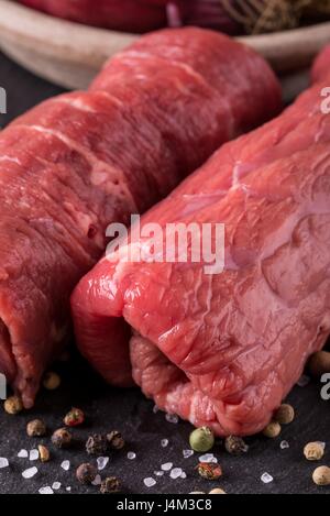 Vertikale Foto mit Details von zwei gerollte Rindfleisch-Scheiben. Fleisch ist für Roulade vorbereitet und auf schwarze Schiefer mit mehreren Gewürzen verschüttet rund um Stockfoto