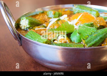 Vegetarische Okra-Curry-Gericht mit frischem Gemüse, serviert im traditionellen Stahl & Messing Schale auf Mahagoni-Tisch. Stockfoto