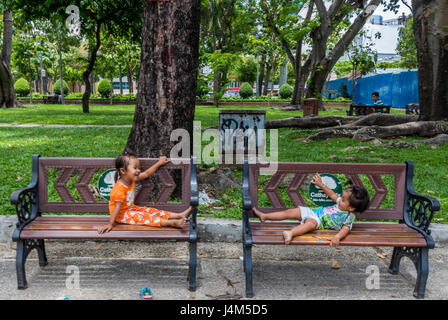 Zwei kleine Kinder spielen auf den Bänken im Park in Saigon Vietnam Stockfoto