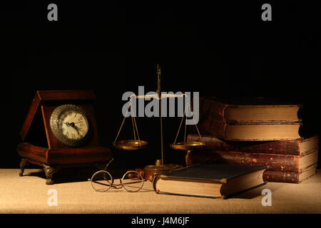 Vintage Holz Uhr in der Nähe von Messing Waage und Bücher auf dunklem Hintergrund Stockfoto