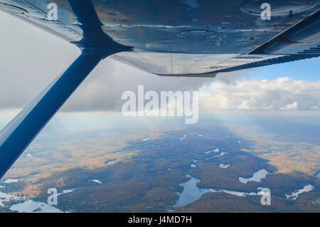 Fliegen ein kleines Flugzeug während der Falljahreszeit an der Basis der Wolken bei 4000 Fuß, Strahlen Bäume und Seen unter mit der Sonne, die Weitergabe durch die Wolken. Stockfoto