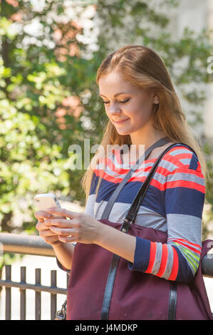 Lächelnd kaukasischen Frau mit Handtasche SMS auf Handy Stockfoto