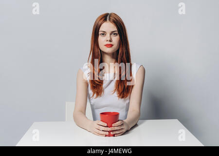 Kaukasische Frau sitzt am Tisch halten rote Tasse Stockfoto