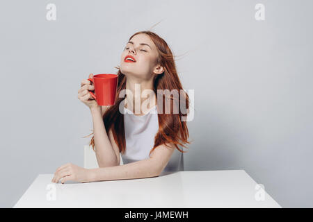 Kaukasische Frau an windigen Tisch halten rote Tasse Stockfoto