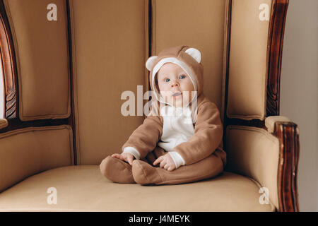 Kaukasische Baby Junge sitzt im Sessel tragen Bär Kostüm Stockfoto