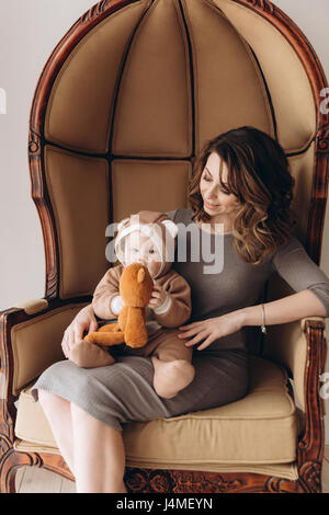 Kaukasische Mutter mit Baby Sohn Bär Kostüm im Sessel sitzen Stockfoto