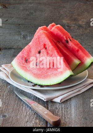 Drei Scheiben Wassermelone auf Teller, Messer auf alten hölzernen Hintergrund Stockfoto