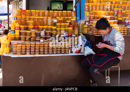 Eine Frau liest die Zeitung, während Gläser frischen natürlichen Honig zum Verkauf an einem Stall in Osh Basar, einem der größten täglichen Märkte Bischkek sind. Kirgistan. Stockfoto