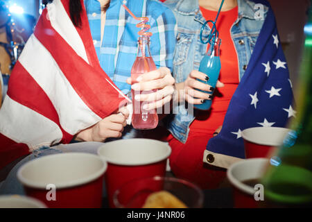 Mittelteil Porträt von zwei Mädchen im Teenageralter tranken Cocktails auf late-Night-Party, eingehüllt in amerikanischen banner Stockfoto