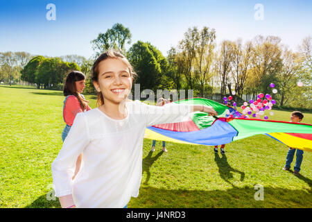 Close-up Portrait von glücklichen Mädchen hält das Seil des Regenbogens Fallschirm im lustigen Spiel im Freien mit Freunden Stockfoto