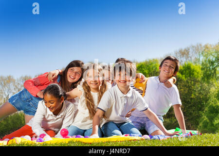 Große Gruppe von glückliche 10-12 Jahre alte Kinder, sitzen auf dem Rasen im Park, umarmen und lachen Stockfoto