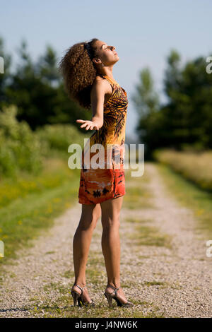 Ziemlich afrikanisch-amerikanische Modell mit lockigem Haar draußen in der Natur in einem orange mini kleid posiert. Stockfoto