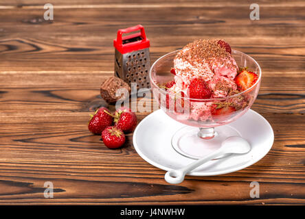 Stil Leben Dessert Erdbeer Rosa Vanilleeis Kugeln mit Reibe, Schokolade und frischen Erdbeeren in Schüssel auf hölzernen Hintergrund Stockfoto