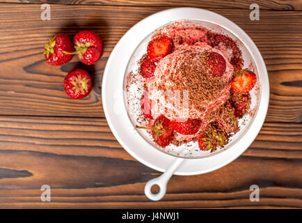 Draufsicht der Dessert Erdbeer Rosa Vanilleeis Kugeln mit bestreut Schokolade und frischen Erdbeeren auf Holztisch Stockfoto