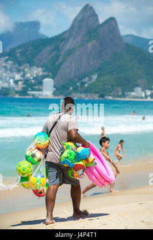 RIO DE JANEIRO - 10. Februar 2017: Ein Strand Anbieter verkaufen bunte Wasserbälle und Spielzeug trägt seine Anzeige am Strand von Ipanema-Strand entlang. Stockfoto