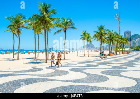 RIO DE JANEIRO - 15. Februar 2017: Ein paar gehen gemeinsam entlang der ikonischen schwarz-weiß Wellenmuster der Promenade am Strand Copacabana. Stockfoto