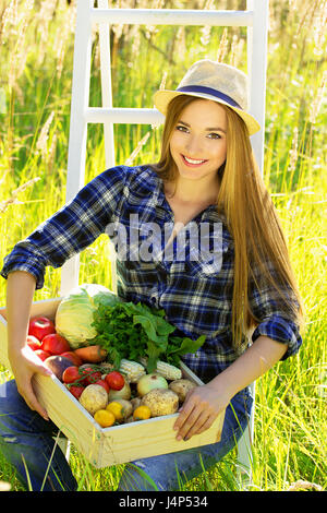 Sommer Ernte in das Dorf auf dem Lande. Junge und schöne Mädchen halten die Box voll mit Gemüse. Stockfoto