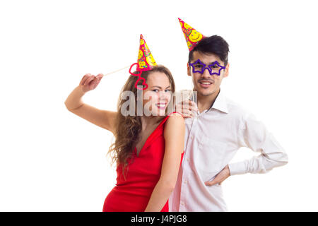 Junge attraktive Frau mit lange kastanienbraunes Haar im roten Kleid und schönen jungen Mann im weißen Hemd mit Feiernden Hüte mit Card-sticks Gläser Stockfoto