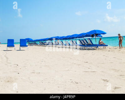 Sunny Isles Beach, USA - 22. März 2011: Viele Liegestühle mit Sonnenschirmen und zwei blauen liegen auf Sand vom Meer in Miami mit Menschen Stockfoto