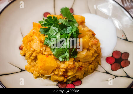 Nahaufnahme von Linsen-Curry mit Kartoffeln, Koriander und Joghurt-Sauce auf Teller Stockfoto