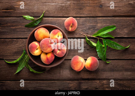 Frische saftige Pfirsiche mit Blättern auf dunklem Holz rustikal Stockfoto