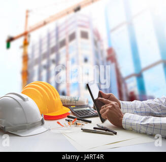 Hand des Architekten arbeiten am Tisch mit Tablet Computer und Arbeit Werkzeugausrüstung gegen Reflexion des Büro Gebäude und Kran Bau für ci Stockfoto