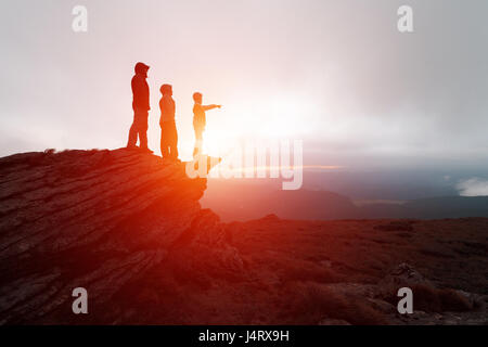 Familie von Touristen, die am Rande der Klippe vor dem Hintergrund einer unglaublichen Berglandschaft. Abendzeit und orange sunset Stockfoto