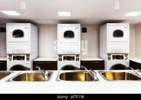 Großen Waschsalon mit Waschmaschine und Trockner hinter Waschbecken mit Armaturen für Kunden mit Wäsche bereit. Stockfoto