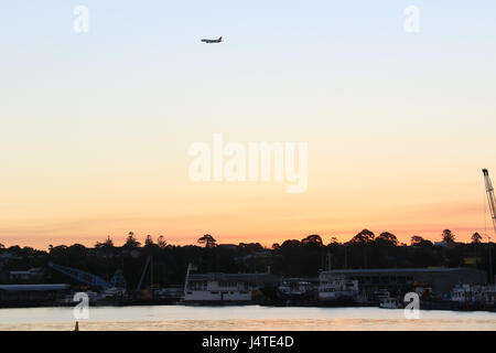 Ein Flugzeug fliegt über Sydneys Inner-West bei Sonnenuntergang von Rozelle Bay ersichtlich. Stockfoto