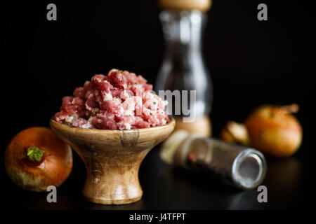 Gehacktes Fleisch in einer Holzschale mit Gewürzen auf schwarzem Hintergrund Stockfoto