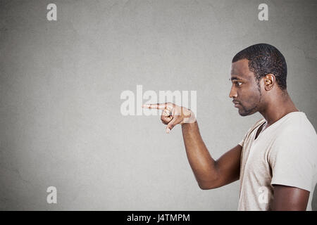 Junge Mann zeigte mit dem Finger auf etwas jemand auf graue Wand Hintergrund Stockfoto