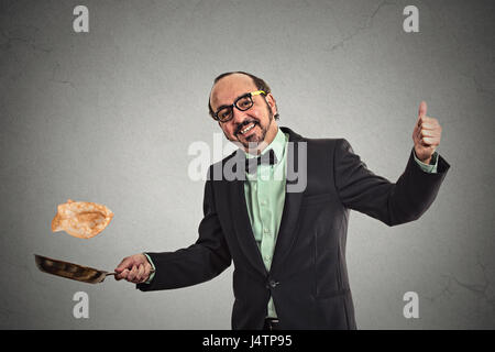 Glücklich lächelnden Mann warf Pfannkuchen auf Pfanne auf graue Wand Hintergrund isoliert. Positive Gesicht Ausdruck Emotion, Küche Spaß Konzept Stockfoto