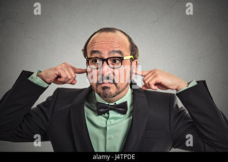 Verärgert reifer Mann mit Brille einstecken Ohren mit den Fingern auf graue Wand Hintergrund isoliert Stockfoto