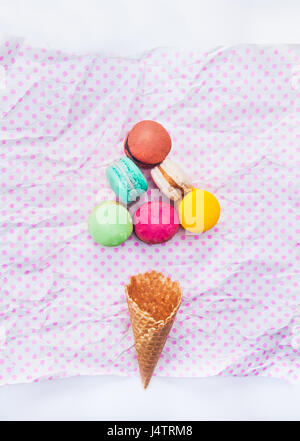 Bunte Kuchen Macarons oder Makronen im Dreieck Form und Waffel Kegel auf weiß mit rosa Erbsen Hintergrund. Ansicht von oben. Freiraum für text Stockfoto