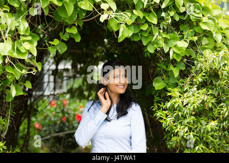 Closeup Portrait zuversichtlich isoliert Lächeln gerne hübsche junge Frau im blauen Hemd genießen einen frischen neuen Tag Hintergrund grüne Sträucher und Blumen Stockfoto