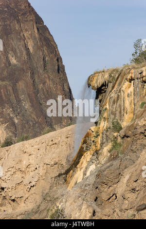 Hammamat Ma Wasserfall von einer felsigen Klippe mit einem zerklüfteten Berg in der Ferne. Blue Sky ist in der Ferne. Wasserfall ist im Profil fotografiert. Stockfoto