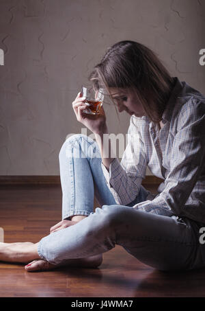 Junge Frau in Depression trinkt Alkohol beim Sitzen auf dem Boden Stockfoto