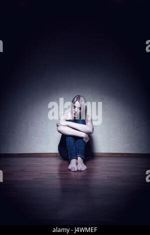 Junge traurige Frau sitzt alleine auf dem Boden in einem leeren Raum Stockfoto