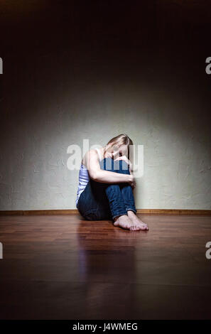Traurige Frau sitzt alleine in einem leeren Raum Stockfoto