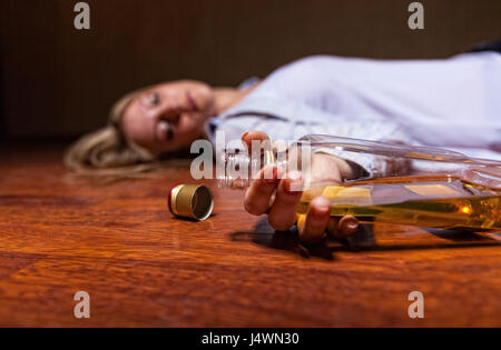 Betrunkene junge Frau auf dem Boden liegend. Die Flasche im Fokus Stockfoto