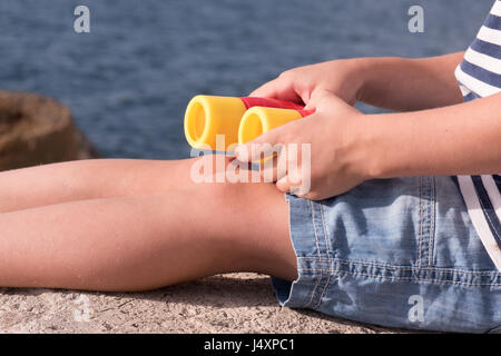 Beine und Hände gesunden kleinen Jungen in kurzen Hosen mit Fernglas auf Meer Hintergrund Stockfoto