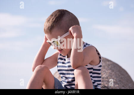 niedlichen kleinen Jungen tragen weiße Sonnenbrille und Sailor Streifen Shirt sitzen Stockfoto