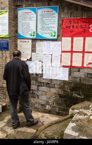 Zhenyuan, Guizhou, China.  Mann liest Mitteilungen veröffentlicht auf der Seite eines Gebäudes. Stockfoto