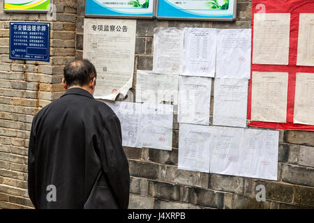 Zhenyuan, Guizhou, China.  Mann liest Mitteilungen veröffentlicht auf der Seite eines Gebäudes. Stockfoto