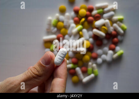 Hand greifen eine weiße Pille aus einem Haufen von Pillen Stockfoto