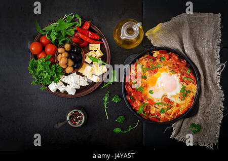 Frühstück. Spiegeleier mit Gemüse - Shakshuka in einer Pfanne auf einem schwarzen Hintergrund im türkischen Stil. Flach zu legen. Ansicht von oben Stockfoto