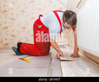junge Handwerker installieren Holzboden im neuen Haus Stockfoto