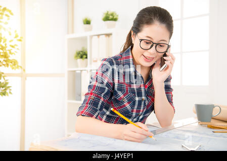 glücklich schönen asiatischen Architektin Frau im Gespräch mit ihren Kunden für ihr Geschäft neue Build Gehäusedesign während an der Rezeption in Crea auf dem Smartphone Stockfoto
