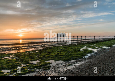 Sonnenaufgang am Bembridge, Isle of Wight, Pier und Boot in der Ferne vergossen, helle grüne Algen rot leuchten in der Sonne Stockfoto